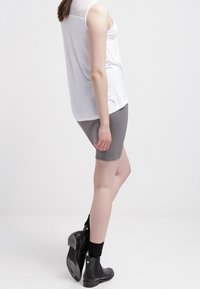 Top bianco senza maniche con dettagli in rete sulle spalle, abbinato a pantaloni corti grigi e stivali alla caviglia neri. Tessuto liscio, vestibilità casual.