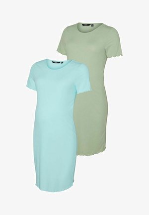 Robe de maternité bleu clair à manches courtes et ourlet festonné. Le mannequin se tient en pose de profil, portant des baskets montantes beiges.