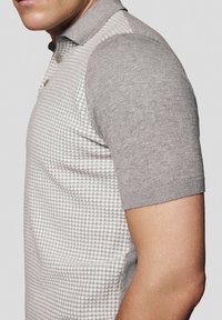 Szary polo z krótkim rękawem o teksturowanym wzorze na korpusie i gładkich rękawach, z kołnierzykiem i dwoma guzikami przy szyi.