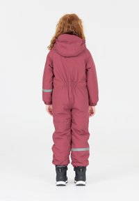 Bordeaux-kleurig sneeuwpak voor kinderen met een capuchon, elastische taille en grijze reflecterende strepen, ontworpen voor buitengebruik. Zwarte schoenen met witte zolen.