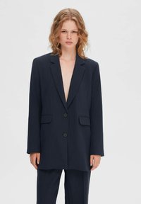 Marineblauwe blazer met scherpe revers, sluiting met knopen aan de voorkant, twee voorzakken en lange mouwen, gemaakt van een gestructureerde stof.