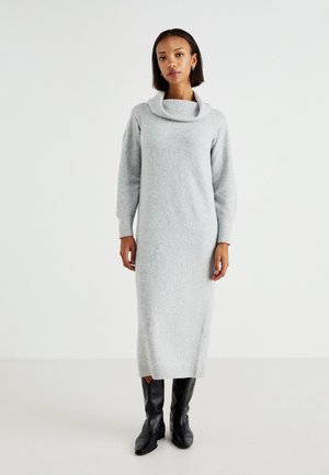 Lungo abito grigio lavorato a maglia con collo a cappuccio e polsini a coste. L'abito ha una silhouette dritta ed è abbinato a stivali neri fino al ginocchio.