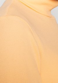 Gestreiftes Turtleneck-Top in Hellorange, mit weicher Textur und enganliegendem Design, das die Nahtdetails an den Schultern hervorhebt.