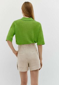 Polo shirt en maille verte à manches courtes, assorti à un short en lin beige avec ourlets et poches arrière.