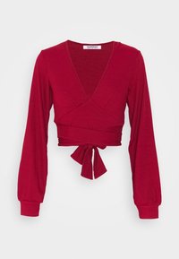 Top cropped vermelho com textura em canelado, decote em V profundo, mangas compridas e detalhe de laço na cintura. Feito de um tecido texturizado e elástico para conforto.