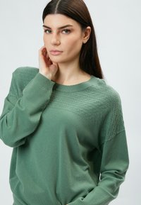 Groen gebreid sweater met een textuurpatroon op de schouders en een zachte, ademende stof. Ronde hals met lange mouwen.