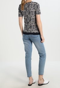 Camiseta de rayas negras y beige con mangas cortas, combinada con jeans azul claro y zapatillas blancas sin cordones. La vista desde atrás muestra una silueta ajustada.