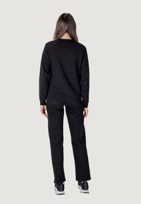 Felpa nera con scollo rotondo e maniche raglan, abbinata a pantaloni neri a gamba dritta. Sneakers grigie completano l'outfit.