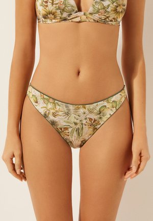 Mujer con bikini de estampado floral con hojas verdes y beige, mostrando la zona media y con las manos relajadas a los lados.