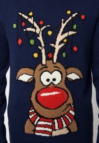 Marineblauwe trui met een rendierontwerp, voorzien van een rode neus, grote ogen en een gestreepte sjaal, versierd met kleurrijke kerstverlichting.