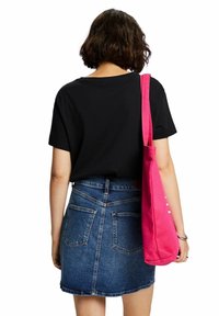 Sort t-shirt med korte ærmer, parret med en denimskørt og en lyserød tote bag. Tasken har en ensfarvet overflade og en skulderrem.