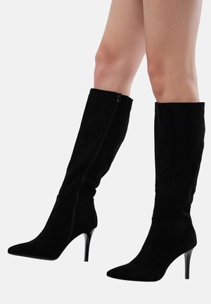 Botas de rodilla de ante negro de tacón alto con puntera afilada y cremallera lateral. El eje es elegante y ajustado, realzando una silueta estilizada.