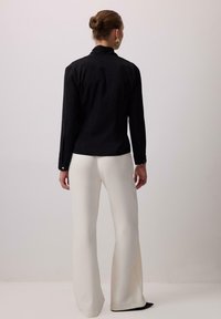 Melnas apkakles krekls ar garām piedurknēm, pieguļoša forma un pogāmas aproces, kombinēts ar baltām izpletu biksēm, gluda tekstūra un neitrāls fons.