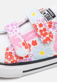 Kolorowe płócienne trampki z kwiatowym wzorem w odcieniach różu, czerwieni i niebieskiego. Posiadają białą bazę, rzepy oraz gumową podeszwę z czarnymi akcentami.