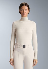 Jasnobeżowy prążkowany sweter z golfem i długimi rękawami. W komplecie z dopasowanymi spodniami z wysokim stanem oraz pasującym, teksturowanym paskiem.