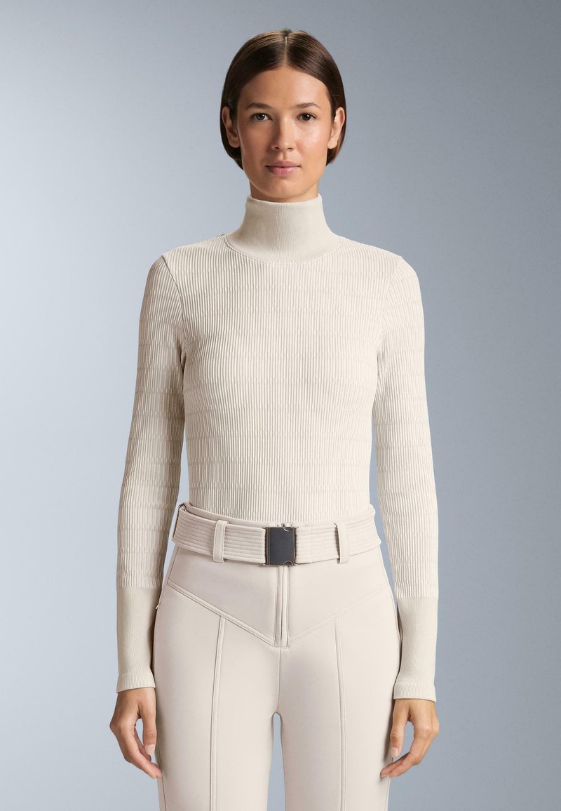 Jasnobeżowy prążkowany sweter z golfem i długimi rękawami. W komplecie z dopasowanymi spodniami z wysokim stanem oraz pasującym, teksturowanym paskiem.