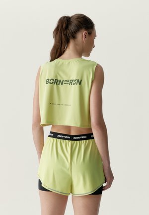 Femme portant un haut court de running vert clair et un short avec des bandes élastiques noires à la taille et le texte "BORN TO RUN" au dos et à la taille.