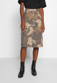 Camo-patterned denim skirt in earth tones with a knee-length cut, featuring a front button closure and a straight silhouette. Worn with black ankle boots.