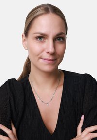 Collana d'argento con piccoli accenti scintillanti, indossata da un modello con una semplice maglietta nera e capelli lisci, braccia incrociate davanti.