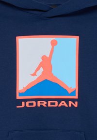 Silueta de un jugador de baloncesto saltando con el balón en la mano extendida, dentro de un cuadrado con fondo azul y gris, texto "JORDAN" debajo.