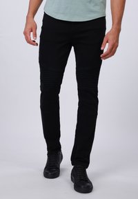 Vaqueros de mezclilla negros con detalles de costura en las rodillas, corte ajustado y una textura suave, combinados con zapatillas negras para un look completo.