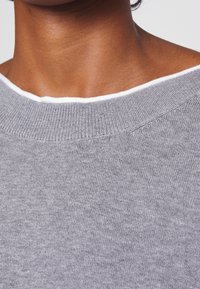 Szary sweter dzianinowy z białym wykończeniem przy dekolcie. Tkanina wydaje się miękka, o delikatnej, jednolitej fakturze i luźnym fasonie.