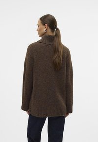 Pull en tricot marron avec un col montant, coupe ample et tissu texturé. Présente des détails côtelés à l'ourlet et aux manches.