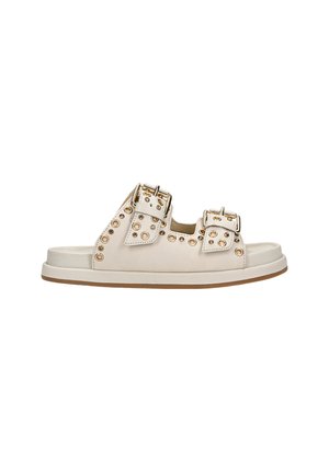 White sandal with two decorative buckles, gold-toned studs along the sides, flat sole, and a simple, open-toe design.