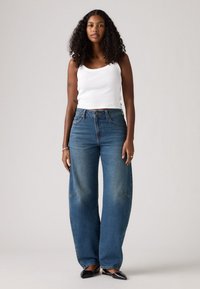 Jean large bleu avec une taille haute et des accents décolorés, associé à un débardeur blanc ajusté. Texture lisse, design décontracté.