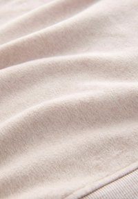 Jasnoróżowa tkanina o miękkiej, teksturowanej powierzchni, z delikatnymi fałdami i gładkim brzegiem. Materiał wygląda na puszysty i przytulny.