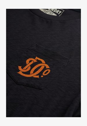 Mørkeblå T-shirt lavet af tekstileret stof med et orange logo på venstre lomme. Udhalsingen er rund, og pasformen er afslappet.