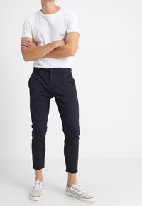 Vit crew-neck t-shirt i kombination med marinvita slim-fit byxor, med en mjuk textur och subtil lyster, kompletterat med ljusa sneakers.