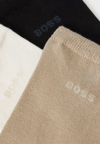 Tris kojinių porų: juodos, bežinės ir kreminės. Pagamintos iš lygaus audinio su raukšlėtomis apykaklėmis. Spausdintas "BOSS" logotipas derančiomis spalvomis.