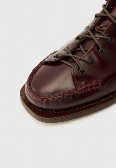 Scarpa in pelle bordeaux scuro con punta arrotondata, cuciture a contrasto e suola in gomma marrone. Presenta lacci e occhielli grigi.