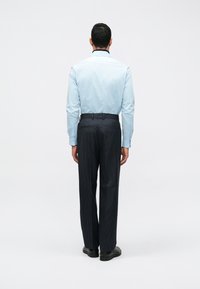 Ljusblå långärmad skjorta, knappad, kombinerad med mörka randiga byxor. Slim fit med en subtil glans, visad bakifrån. Svarta skor.