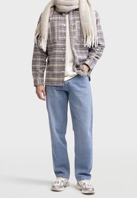 Košile s kostkovaným vzorem v béžové, modré a bílé, přeložená přes bílý tričko; doplněná o světle modré volné džíny a vzorované tenisky.