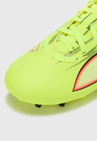 Bota de fútbol amarillo neón con superficie texturizada, tachones negros y detalles en rojo brillante. Presenta un diseño aerodinámico y cordones planos.