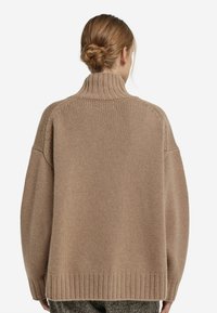 Beżowy sweter z dzianiny z wysokim kołnierzem, opadającymi ramionami oraz ściągaczami przy mankietach i u dołu. Miękka faktura i luźny krój. Widoczne wzory ściegów.
