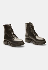 Stivali ankle in pelle nera con finitura texture, design con lacci e cerniera laterale. Suola spessa con battistrada pronunciato per una maggiore trazione.