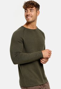 Pull en maille côtelée de couleur vert olive, à manches longues, avec un col rond et une coupe ajustée. Il se distingue par ses manches raglan et un motif horizontal subtil.
