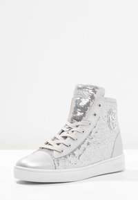 Vysoké tenisky s povrchem z stříbrných flitrů, kovovou špičkou a světle šedými akcenty. Obsahují ploché tkaničky a vyražené logo.