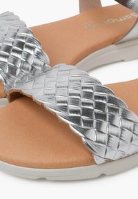 Sandali con cinturini intrecciati in argento, dotati di un plantare imbottito color ocra e suola in gomma bianca. I cinturini presentano un design intrecciato con finitura lucida.