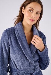 Accappatoio blu in peluche con un motivo testurizzato e colletto a scialle. Presenta una vita con cintura e maniche lunghe. Tessuto morbido con finitura liscia.