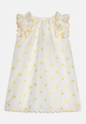 Bijela haljina bez rukava sa žutim točkicama, naboranim detaljima na ramenima i valovitim rubovima s žutim obrubom.