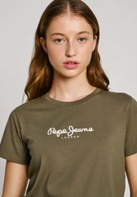 Olivinės spalvos medvilninė marškinėliai su trumpomis rankovėmis, apvaliu iškirpimu ir balta "Pepe Jeans London" logotipu spausdintu priekyje. Lygus paviršius.