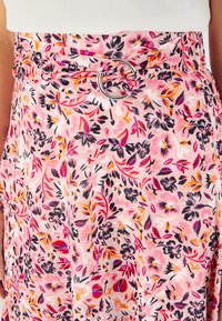 Falda floral de tela rosa clara con una mezcla de flores negras, moradas y naranjas. Acentuada con un hebilla circular plateada.