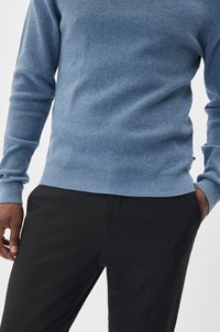 Light blue knit sweater with a textured finish and ribbed cuffs, paired with black trousers. Sweater has a subtle design at the hem.