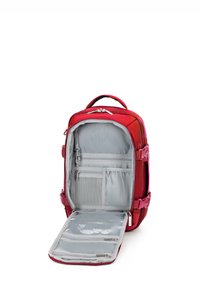 Červený látkový batoh s šedým interiérem. Má několik přihrádek, včetně síťové kapsy, zipů a plochého, otevřeného předního víka.
