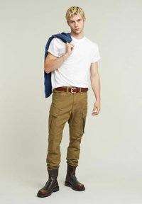 Tan cargobroeken met meerdere zakken, een wit T-shirt en zwarte leren laarzen. Een blauwe denimjas hangt over de schouder.