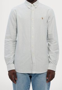 Camicia a righe con bottoni realizzata in un misto cotone. Strisce azzurro chiaro e bianche, chiusura con bottoni e un piccolo logo sulla tasca sinistra del petto.